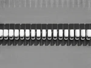 Witte bedrijfsvoertuigen in perfecte rij op grijze parkeerplaats, bovenaanzicht met geometrische schaduwen