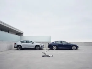 Elektrisch voertuig en conventionele sedan geparkeerd naast elkaar in modern parkeerterrein, laadkabel op de grond.