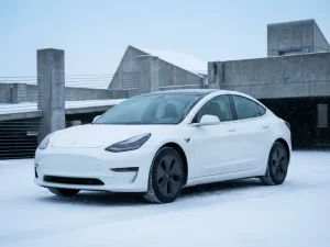 Witte elektrische auto geparkeerd op besneeuwde moderne parkeerplaats met rijp op voorruit en spiegels