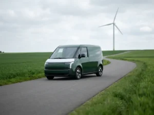Elektrisch vlootvoertuig op een open weg tussen groene velden, met een witte windturbine op de achtergrond.
