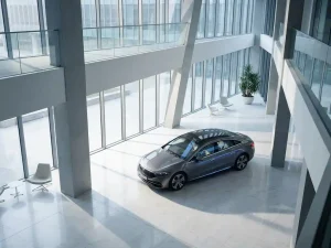 Elektrische sedan geparkeerd in minimalistische lobby met glazen wanden, natuurlijk licht en marmeren vloeren