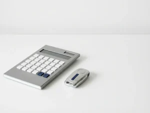 Strakke calculator met geometrische knoppen naast metalen autosleutel op wit bureau, zachte schaduwen en minimalistische vormgeving
